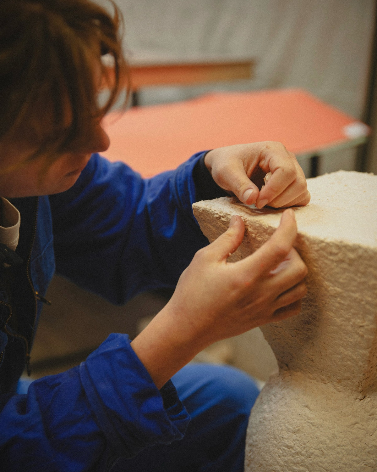 A maker refining the edge of a papier-mâché plinth by hand.